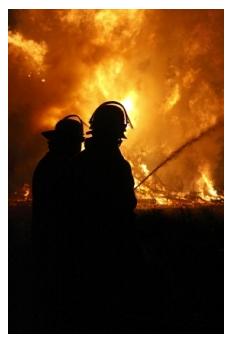 fire fighters battling a blaze with fire in background